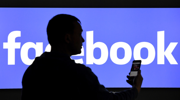 Ein Mann mit Smartphone steht vor einem Monitor mit dem Logo von Facebook. Foto: Carsten Rehder/dpa