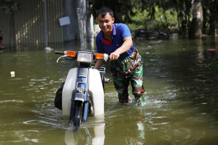 Ein Vietnamese schiebt sein Motorrad durch die Wassermassen. Foto: epa/Luong Thai Linh