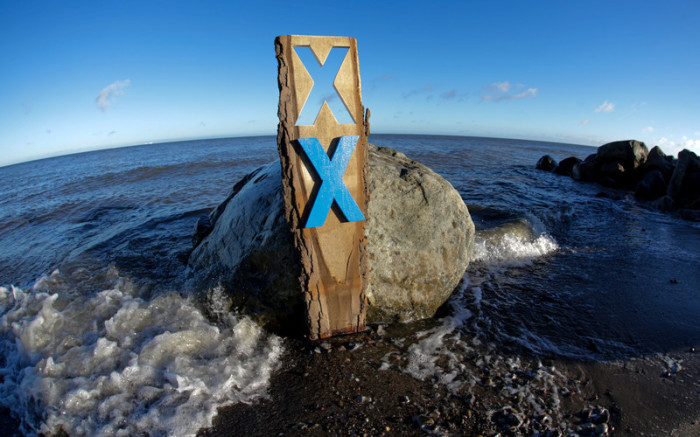Eine Holzplanke mit einem blauen Kreuz als Widerstandszeichen wird am Strand von Fehmarn aufgestellt. Foto: epa/Axel Heimken