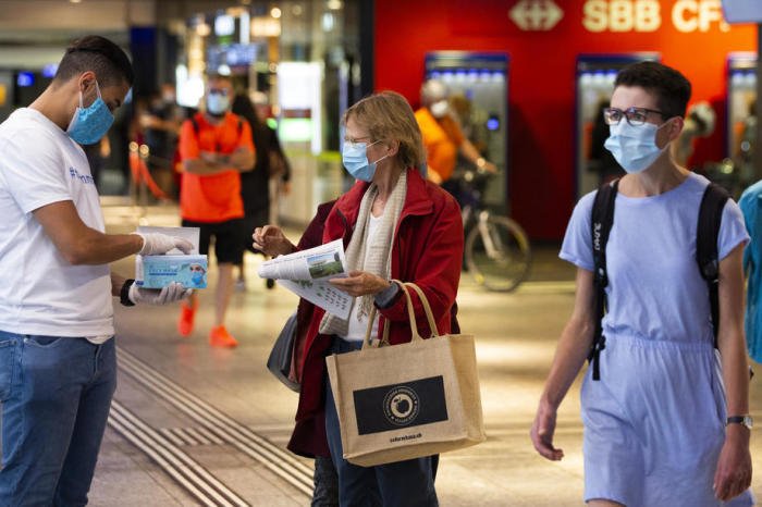 Freiwilliger verteilt Gesichtsmasken an Fahrgäste im Hauptbahnhof in Bern. Foto: epa/Peter Klaunzer