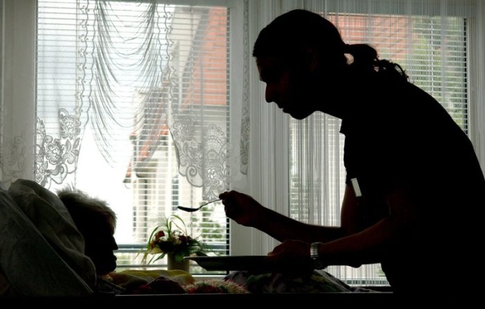 In einem Seniorenheim füttert ein Mitarbeiter eine Bewohnerin die im Bett liegt. Foto: Patrick Pleul/Dpa-zentralbild/dpa