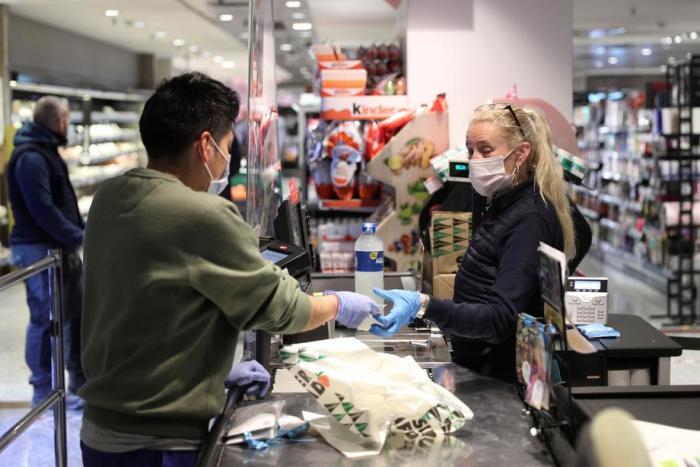 Ein Shopper (L), der eine Gesichtsmaske und Handschuhe trägt, bezahlt seine Einkäufe in einem Supermarkt in Madrid. Foto: epa/Rodrigo Jimenez