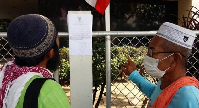 Zwei Protestler lesen einen Zettel der Polizei, der über das Versammlungsverbot am Regierungssitz informiert. Foto: The Nation