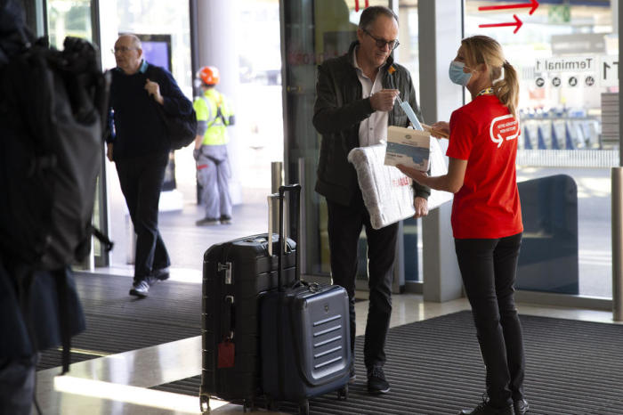 Eine Mitarbeiterin des Genfer Flughafens gibt den Passagieren in der Abfertigungshalle des Terminals 1 am Genfer Flughafen einen Gesichtsschutz. Foto: epa/Salvatore Di Nolfi
