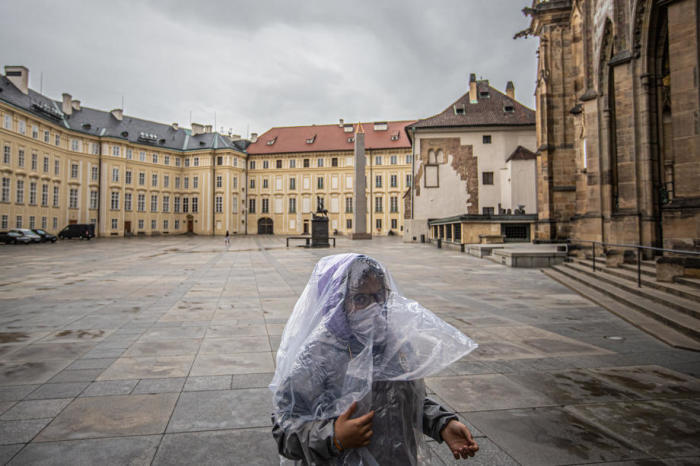 Ein Besucher, der eine schützende Gesichtsmaske trägt und vor dem Regen geschützt ist, geht im leeren Viereck auf der Prager Burg in Prag.Foto: epa/Martin Divisek