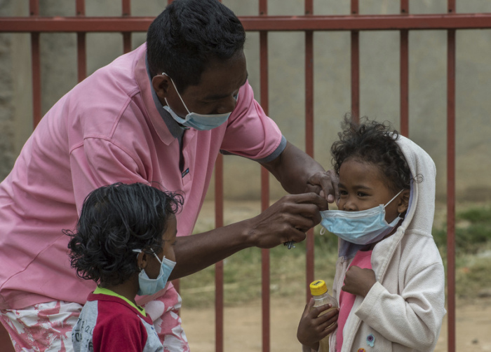 Ein Mann hilft am 03.10.2017 in Antananarivo (Madagaskar) einem Kind beim Anlegen eines Mundschutzes. Immer mehr Menschen infizieren sich auf Madagaskar mit der lebensgefährlichen Lungenpest. Foto: dpa/Alexander Joe/AP