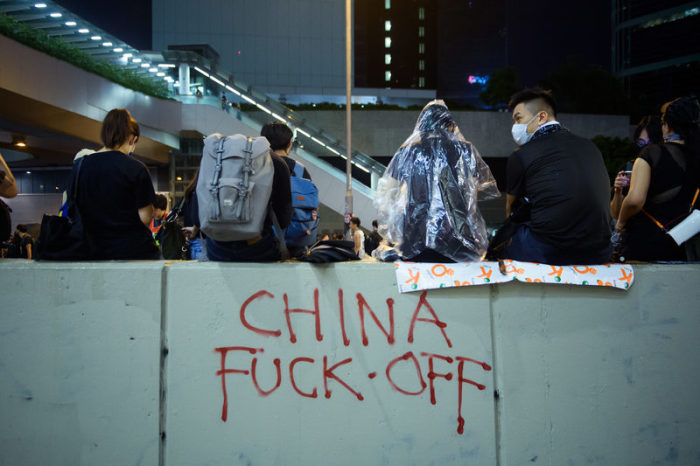 Demonstranten sitzen am Abend auf einer Mauer, die mit einem Grafitti (