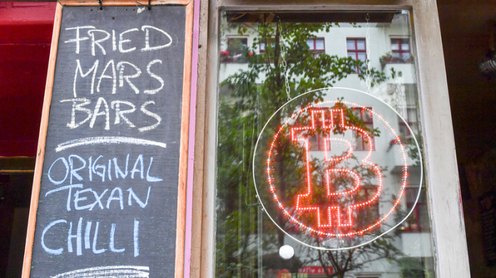 Ein Bitcoin-Logo hängt im Schaufenster der Bitcoin-Kneipe Room 77 im Kreuzberger Graefekiez. Foto: Jens Kalaene/Dpa-zentralbild/dpa