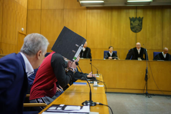 Der irakische Angeklagte Taha Al-J. (2-L), der sein Gesicht mit einer Mappe bedeckt, nimmt vor der Urteilsverkündung in seinem Prozess vor dem Oberlandesgericht Frankfurt am Main im Gerichtssaal Platz. Foto: epa/Frank Rumpenhorst