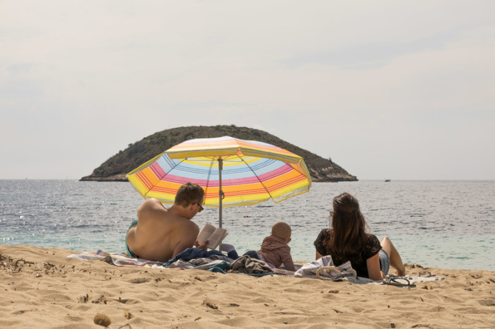 Eine Familie liegt unter einem Sonnenschirm am fast leeren Strand von Magaluf auf Mallorca. Foto: John-patrick Morarescu