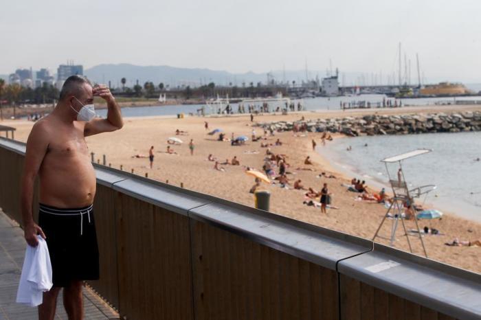 Ein Mann mit einer schützenden Gesichtsmaske blickt auf den Strand Barceloneta. Foto: epa/Marta Perez