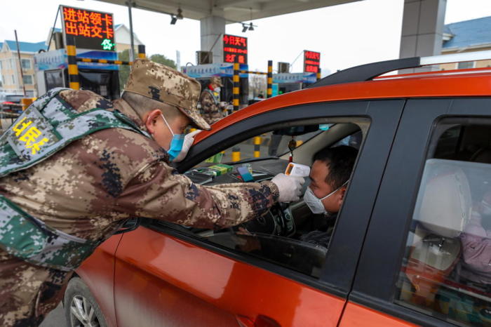 Ein Milizbeamter überprüft die Körpertemperatur eines Fahrers eines Fahrzeugs an einer Autobahnmautstelle in Wuhan. Foto: epa/China Out