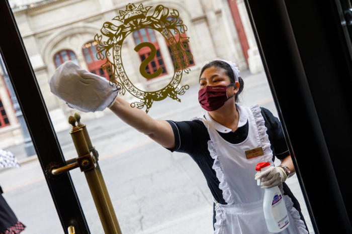 Eine Putzfrau mit Gesichtsmaske reinigt den Haupteingang des traditionellen Hotels Sacher in Wien. Foto: epa/Florian Wieser