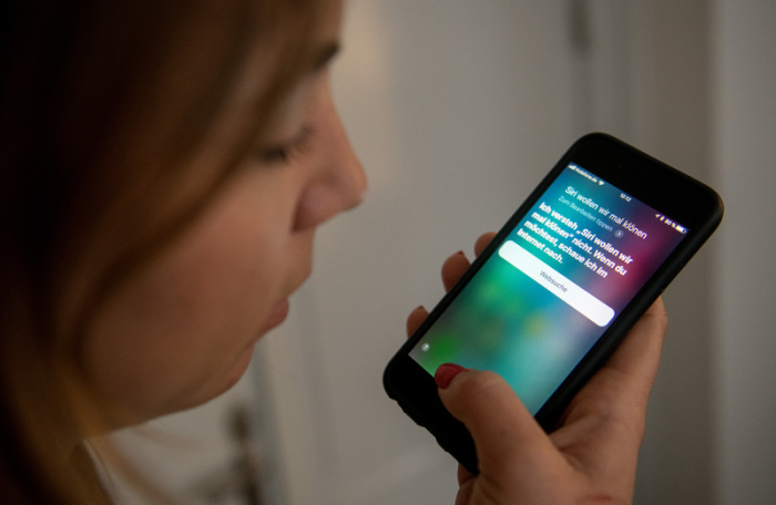 Eine junge Frau bedient auf einem iPhone die Spracherkennung des Apple-Programms Siri. Foto: Daniel Reinhardt/Dpa