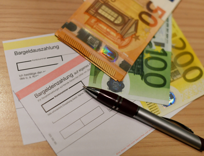 Geldscheine und Bargeldein- und Bargeldauszahlungs Belege liegen an einem Schalter einer Bankfiliale. Foto: Angelika Warmuth/Dpa 