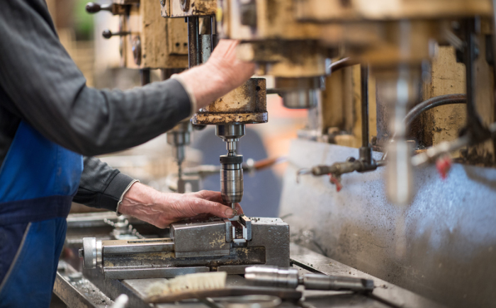 Ein Mitarbeiter bedient in der Produktionshalle einer Firma eine Maschine zur Verarbeitung von Metall. Foto: Monika Skolimowska/Zb/dpa