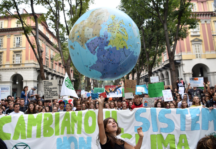 Teilnehmer einer Demonstration halten Transparente, Protestplakate und einen großen Plastikglobus. Foto: Alessandro Di Marco/Ansa/dpa