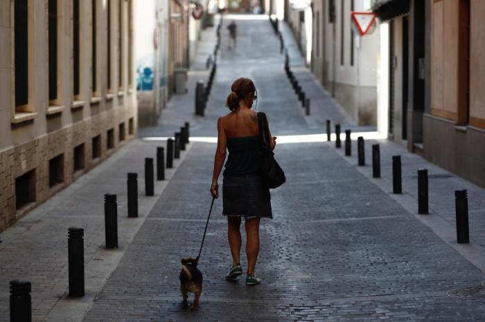 Eine Frau geht an einem heißen Tag in der Madrider Innenstadt mit ihrem Hund durch eine leere Straße. Foto: epa/Mariscal
