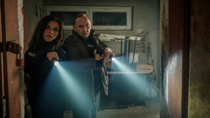 Nina Petersen (Katharina Wackernagel) und Karl Hidde (Alexander Held) beleuchten mit Taschenlampen eine verlassene Lagerhalle in dieser Szene des TV-Krimis 