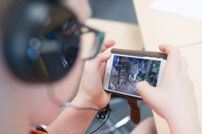 Ein Schüler sitzt am Rande einer Eröffnungsveranstaltung mit Kopfhörern in einem Klassenzimmer der Universitätsschule und spielt auf einem Smartphone ein Videospiel. Foto: Sebastian Kahnert/Zb/dpa