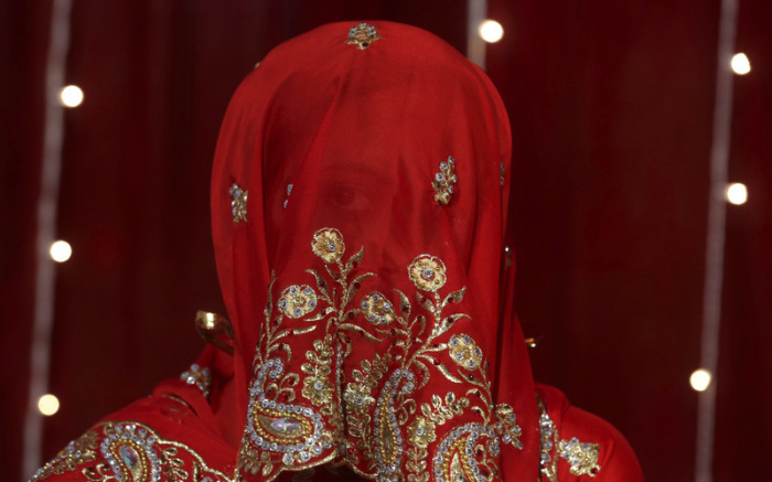 Eine Braut blickt durch ihren Schleier während einer Massenhochzeit. Foto: Rafiq Maqbool