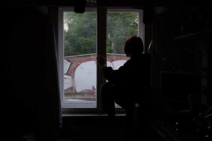 Eine Jugendliche sitzt in einem abgedunkelten Zimmer am Fenster. Die Zahl psychischer Erkrankungen hat durch die Corona-Pandemie weltweit enorm zugenommen (Gestellte Szene). Foto: Paul Zinken/dpa