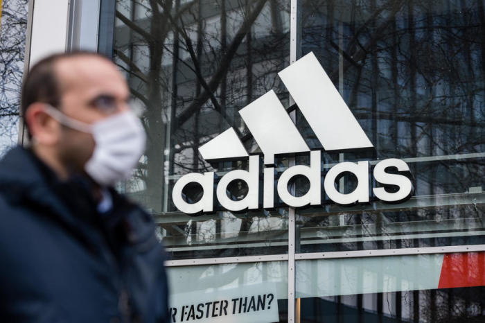 Ein Mann mit Schutzmaske vor einem adidas-Store mit dem Logo des Sportartikelherstellers, in Berlin. Foto: epa/Jens Schlueter