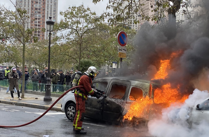 Ein Feuerwehrmann löscht ein von «Gelbwesten»- Demonstranten in Brand gesetztes Auto. Foto: Kong Fan/Xinhua/dpa