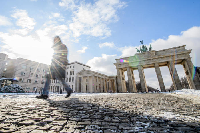 eine Frau geht auf dem menschenleeren Pariser Platz vor dem Brandenburger Tor in Berlin spazieren. Foto: epa/Clemens Bilan