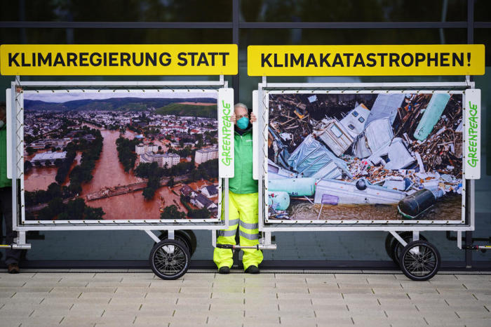 Ein Aktivist der Umweltorganisation Greenpeace steht während der Koalitionsverhandlungen zwischen Fotos, die Klimakatastrophen zeigen. Foto: epa/Clemens Bilan