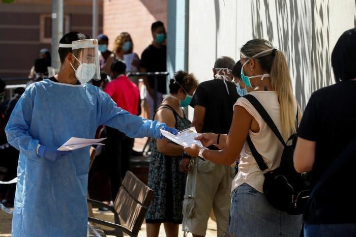 Ein Mitarbeiter des Gesundheitswesens informiert die Menschen, die in einem Gesundheitszentrum in Canovellas, Barcelona, Schlange stehen. Foto: epa/Quique Garcia