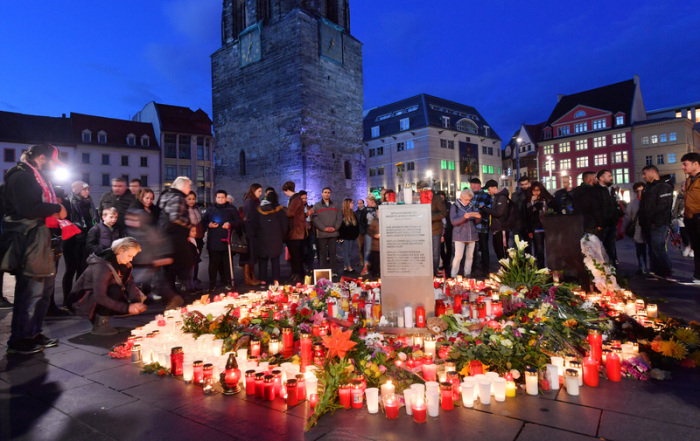Menschen stehen in der Abenddämmerung auf dem Marktplatz neben Blumen und Kerzen, um ein Zeichen gegen Gewalt zu setzen und um zu Trauern. Foto: Hendrik Schmidt/Dpa
