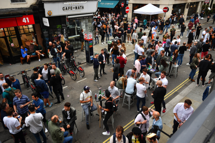Menschen versammeln sich zum gemeinsamen Trinken auf einer Straße vor Bars im Stadtteil Soho. Nach mehr als drei Monaten Schließung wegen der Corona-Pandemie haben die Pubs in England wieder geöffnet. Foto: Victoria Jones/Pa Wire/dpa