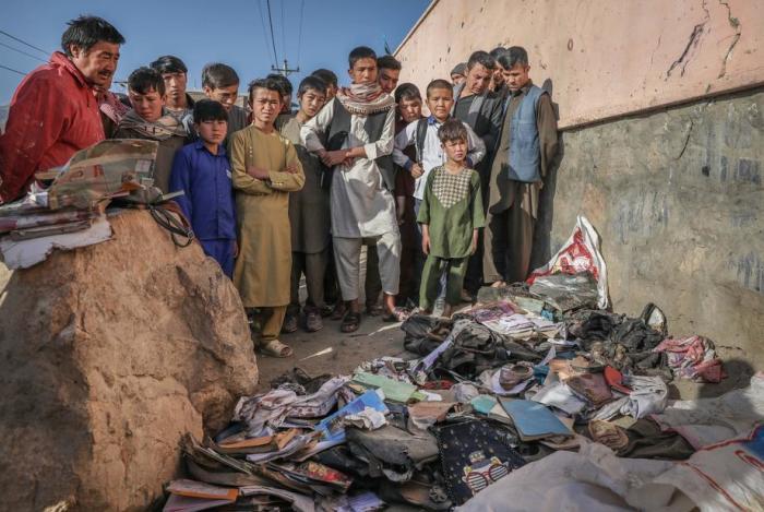 Afghanische Menschen bewachen die Habseligkeiten der Opfer, wie die blutbefleckten Bücher und Hefte der Schüler zu sehen sind.