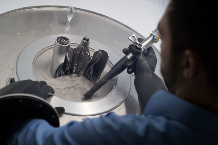Ein Mitarbeiter saugt im 3D-Druck-Applikationszentrum des Maschinenbauers Trumpf in einer Entpackstation Metallpulver von einem im 3D Druck gefertigten Bauteil. Foto: Marijan Murat/Dpa