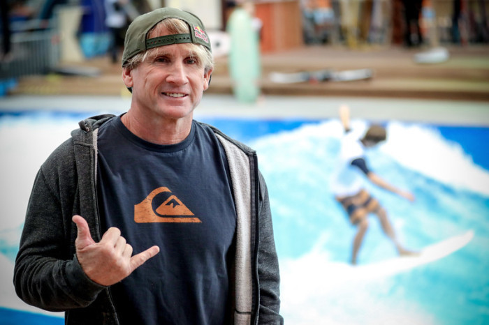 Der US-amerikanische Surfer und mehrfache Windsurfing-Weltmeister Robert 'Robby' Naish posiert für ein Foto, während ein Surfer auf einer stationären Tiefwasserwelle reitet. Foto: epa/Friedemann Vogel