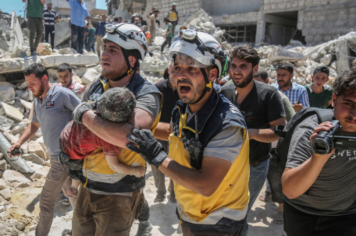 Weißhelme des syrischen Zivilschutzes tragen ein verletztes Kind aus den Trümmern eines zerstörten Gebäudes. Foto: Anas Alkharboutli/Dpa
