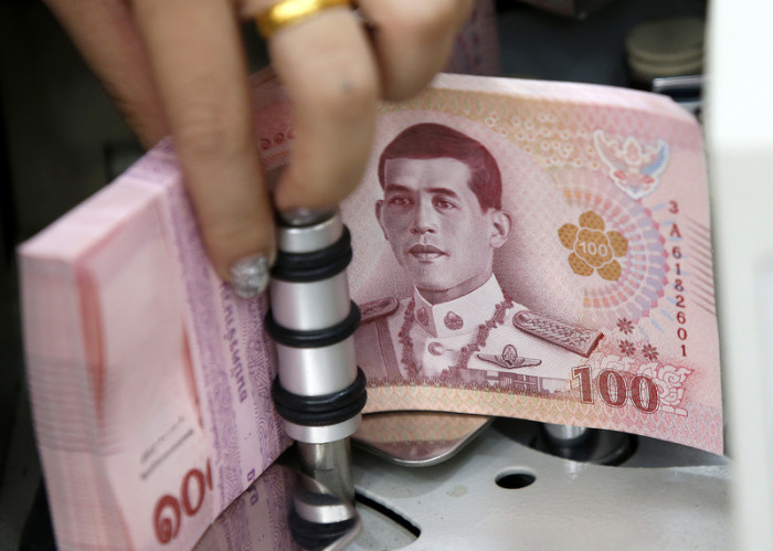Eine Bankangestellte befüllt eine Geldzählmaschine mit 100-Baht-Banknoten. Foto: epa/Narong Sangnak
