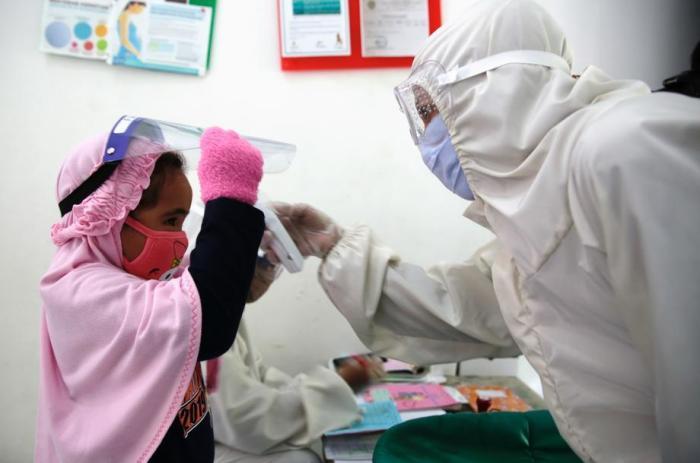Eine Krankenschwester im Schutzanzug prüft in einem Impfstoffhaus in Depok die Körpertemperatur eines Mädchens. Foto: epa/Adi Weda