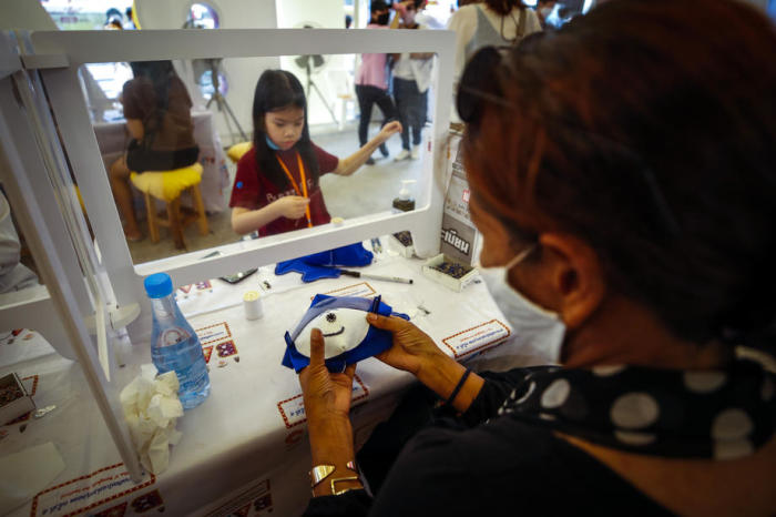 Bei der Herstellung von Gesichtsschutzmasken für Kinder mit Tüchern auf einer Messe in Bangkok werden die Menschen durch Plastiktrennwände getrennt, um ein Minimum an sozialer Distanzierung zu gewährleisten. Foto: epa/Diego Azubel