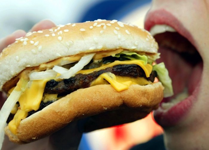 Eine junge Frau isst einen Hamburger. Neben einer wachsenden Weltbevölkerung könnte auch das steigende Gewicht der Menschen den globalen Bedarf an Kalorien aus Lebensmitteln zusätzlich erhöhen. Foto: Gero Breloer/Dpa