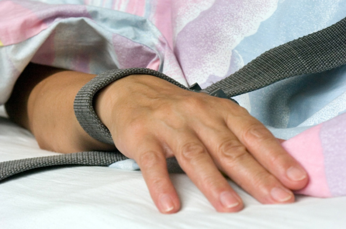Eine mit einem Textilband festgebundene Hand eines Patienten - die Fixierung bzw. Fixation eines Patienten in der Krankenpflege durch Festschnallen am Handgelenk. Foto: dpa/Hans Wiedl