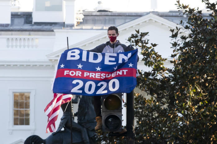 Ein Biden-Unterstützer hält eine Flagge, während er auf einer Ampel sitzt. Foto: epa/Michael Reynolds