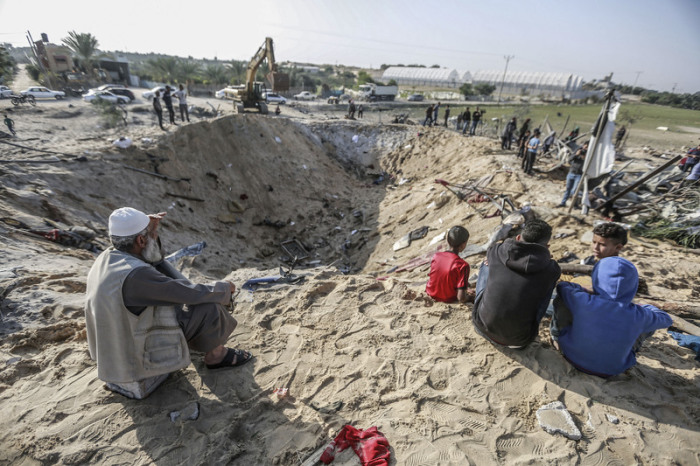 Palästinenser sitzen an einem Krater, der bei einem israelischen Luftangriff entstanden ist. Foto: Mohammed Talatene/Dpa