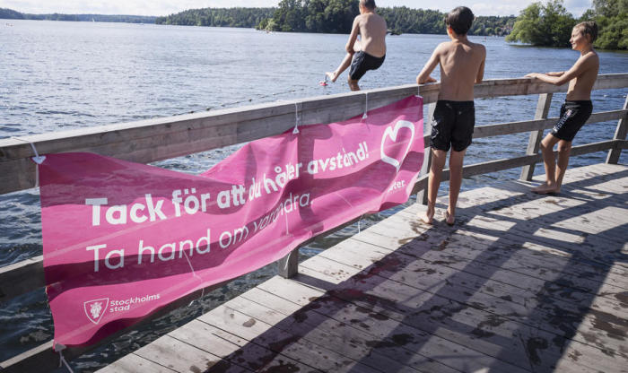 Die Jungen genießen einen sonnigen Sommertag am Malaren-See, während in Stockholm inmitten des Ausbruchs der Coronavirus-Krankheit (COVID-19) ein soziales Distanzschild an einem Zaun hängt. Foto: epa/Naina Helen Jama