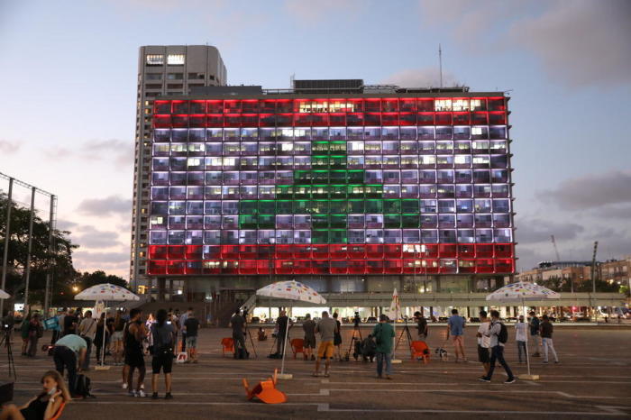 Die Menschen schauen auf das Gebäude der Stadtverwaltung von Tel Aviv, das mit den Farben der libanesischen Flagge beleuchtet ist. Foto: epa/Abir Sultan