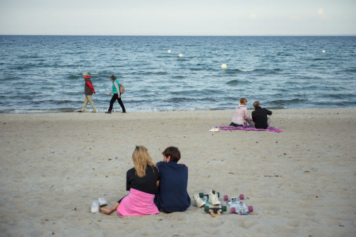 Paare sitzen und gehen in einigem Abstand zueinander am Strand der Gemeinde Scharbeutz im Kreis Ostholstein. Foto: Gregor Fischer/dpa