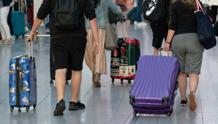 Reisende gehen im Flughafen Düsseldorf mit Koffern durch die Abflughalle. Foto: Henning Kaiser/dpa