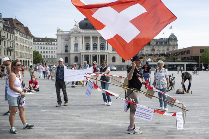 Ein Mann mit selbstgebasteltem Abstandshalter und einer Schweizer Nationalflagge nimmt an einem Protest gegen die Corona-Beschränkungen auf dem Sechseläutenplatz teil. Foto: Ennio Leanza/Keystone/dpa