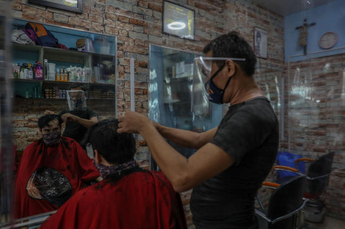Friseur Chris (R) trägt einen Gesichtsschutz, während er in einem Salon inmitten der Coronavirus-Pandemie in Manila die Haare von Rad (L) zwischen Plastikplanen schneidet. Foto: epa/Mark R. Cristino